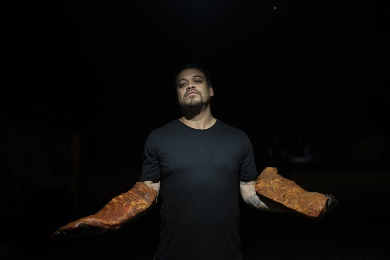 Miguel Vidal holds a slab of ribs and brisket while smoking meats in the middle of the night at his restaurant, Valentina's Tex Mex BBQ, in the early hours of Sunday, April 23, 2023, in Austin, Texas. Later in the year, the restaurant re-opened in Buda, a suburb south of the capital. "When you think back in history to the cattle trade moving through Texas, it's what made Texas, what Texas is," Vidal said. "Brisket is king in the barbecue restaurants." (AP Photo/David Goldman)