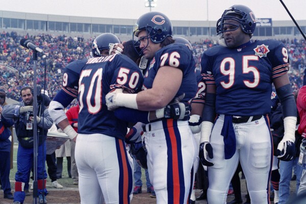 FILE - Chicago Bears nine-time Pro Bowler Mike Singletary (50) gets a bear hug from teammate Steve McMichael (76) prior to an NFL football game against the Pittsburgh Steelers in Chicago, Dec. 13, 1992. Chicago Bears great Steve McMichael, who's battling ALS, was hospitalized again and undergoing tests Wednesday, April 3, 2024, publicist Betsy Shepherd said.. (AP Photo/David Boe, File)