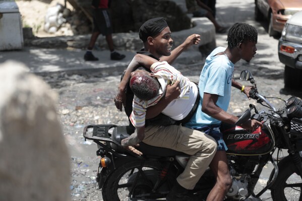 A police officer holds a resident who was shot in the head during violent gang clashes, as he carries him away on a moto-taxi in the Carrefour-Feuilles district of Port-au-Prince, Haiti, Tuesday, Aug. 15, 2023. (AP Photo/ Odelyn Joseph)