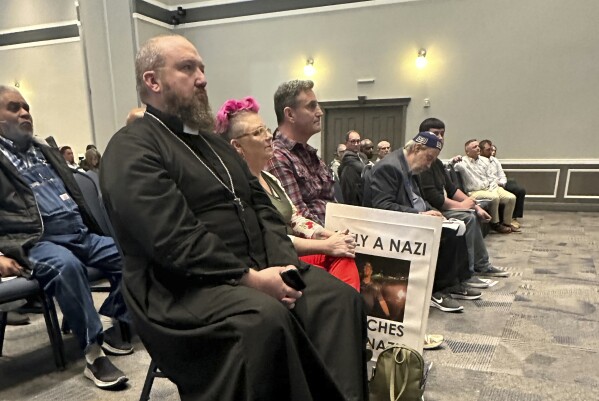 Father James Neal, foreground, pastor of the Holy Cross Orthodox Catholic Church in Enid, Okla., listens during a community forum in Enid, Tuesday, March 26, 2024. Judd Blevins, who has acknowledged ties to white supremacist groups, is facing a recall vote in Enid, Tuesday, April 2, 2024. (AP Photo/Sean Murphy)