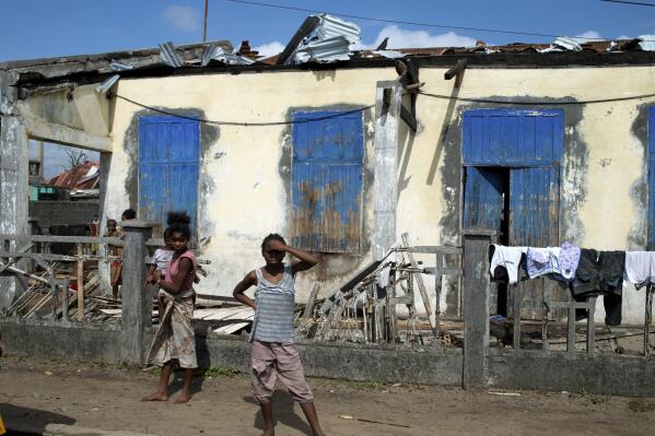 FILE — People stand outside a ruined home in Mananjary, Madagascar Thursday, Feb. 10, 2022. Even as southern African nations assess the devastation caused earlier this month by Cyclone Batsirai, a new tropical storm is approaching as the Indian Ocean region is confronted by an intense cyclone season. (AP Photo/Viviene Rakotoarivony.File)