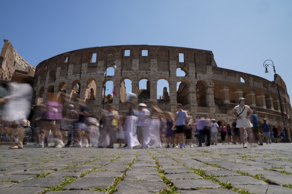 Visitors walk past the Colosseum, in Rome, Tuesday, June 27, 2023. Italy's culture and tourism ministers Gennaro Sangiuliano vowed to find and punish a tourist who was filmed carving his name and his girlfriend's name in the wall of the Colosseum, a crime that in the past has resulted in hefty fines. Video of the incident went viral on social media, at a time when Romans have already been complaining about hordes of tourists returning to peak season travel this year. (AP Photo/Andrew Medichini)