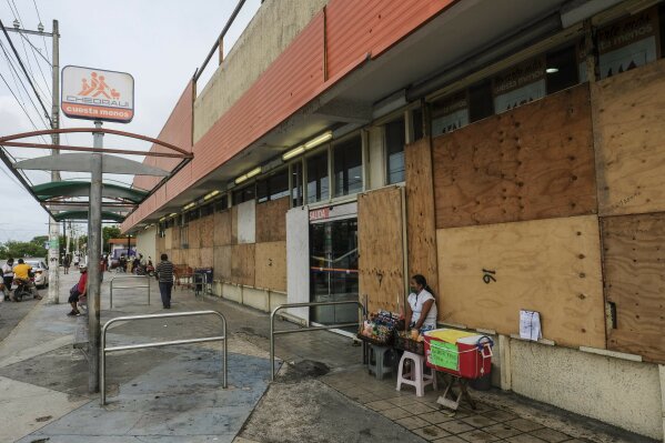 A woman waits for clients outside a supermarket with its windows covered with plywood as Tropical Storm Zeta approaches Cancun, Mexico, Monday, Oct. 26, 2020. A strengthening Tropical Storm Zeta is expected to become a hurricane Monday as it heads toward the eastern end of Mexico's resort-dotted Yucatan Peninsula and then likely move on for a possible landfall on the central U.S. Gulf Coast at midweek. (AP Photo/Victor Ruiz Garcia)