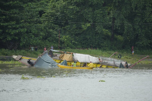People inspect a capsized ferry in Binangonan, Rizal province, Philippines, Friday, July 28, 2023. The boat turned upside down on Thursday when passengers suddenly crowded to one side in panic as fierce winds pummeled the wooden vessel, killing a number of people, officials said Friday. (AP Photo/Aaron Favila)