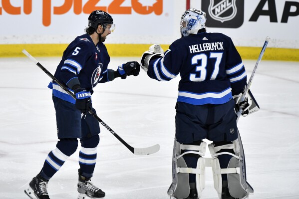 Winnipeg Jets' Brenden Dillon (5) celebrates his goal against the Columbus Blue Jackets with goaltender Connor Hellebuyck (37) during the first period of an NHL hockey game Tuesday, Jan. 9, 2024, in Winnipeg, Manitoba. (Fred Greenslade/The Canadian Press via AP)