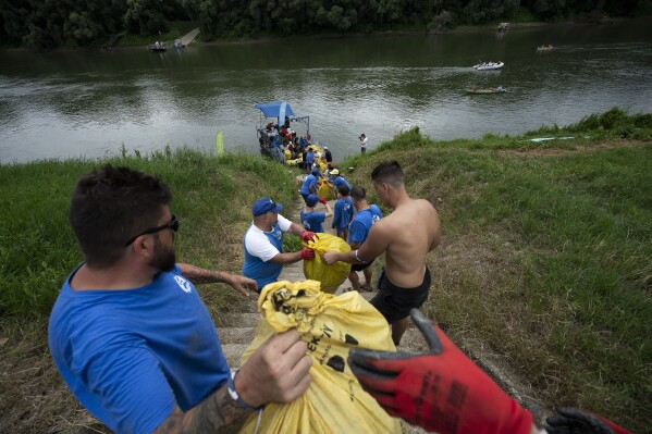 Voluntários formam uma corrente viva para facilitar o despejo do lixo coletado naquele dia na praia enquanto participam do evento Plastic Cup perto de Tiszaroff, Hungria, terça-feira, 1º de agosto de 2023. (AP Photo/Denes Erdos)