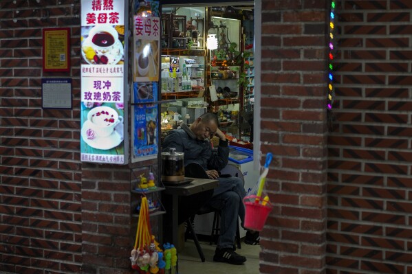 A man browses his smartphone at his store in Xiamen in southeast China's Fujian province on Dec. 27, 2023. A survey of factory managers in China shows manufacturing contracted in December in the latest sign the world's second-largest economy remains sluggish. (AP Photo/Andy Wong)