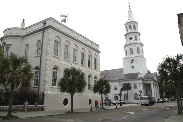 FILE - In an April 7, 2014 file photo, pedestrians walk by City Hall and St. Michael's Episcopal Church in Charleston, S.C. The historic South Carolina city of Charleston has elected its first Republican mayor since the Reconstruction Era. William Cogswell, formerly a Republican state lawmaker, defeated incumbent Democratic Mayor John Tecklenburg by about 2 percentage points in Tuesday, Nov. 21, 2023 runoff, according to the South Carolina Election Commission. (AP Photo/Bruce Smith, file)