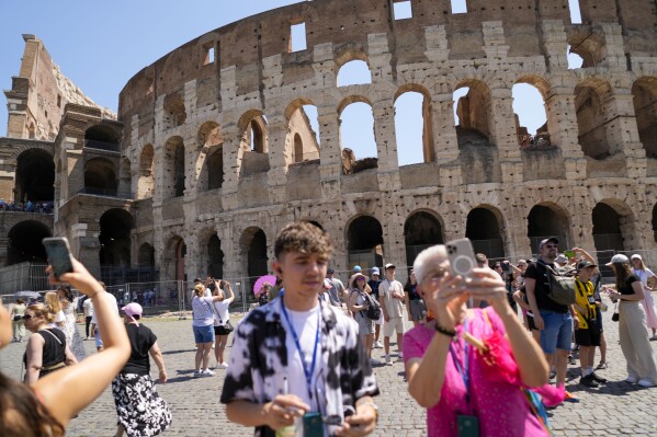 Visitors take photos of the Ancient Colosseum, in Rome, Tuesday, June 27, 2023. Italy's culture and tourism ministers Gennaro Sangiuliano vowed to find and punish a tourist who was filmed carving his name and his girlfriend's name in the wall of the Colosseum, a crime that in the past has resulted in hefty fines. Video of the incident went viral on social media, at a time when Romans have already been complaining about hordes of tourists returning to peak season travel this year. (AP Photo/Andrew Medichini)