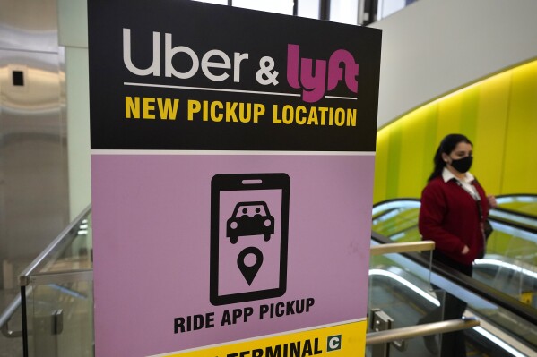 FILE - In this Feb. 9, 2021 file photo, a passer-by walks past a sign offering directions to an Uber and Lyft ride pickup location at Logan International Airport, in Boston. Lyft and Uber are threatening to halt operations in Minneapolis because of a city ordinance to increase wages for app-based drivers, the latest back-and-forth that underscores a longtime fight between gig economy workers and the tech giants.(AP Photo/Steven Senne, File)