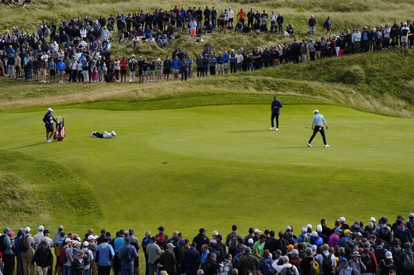United States' Jordan Spieth, right looks back as England's Matt Fitzpatrick lies on the ground to look at the line of his putt on the 12th green during the second day of the British Open Golf Championships at the Royal Liverpool Golf Club in Hoylake, England, Friday, July 21, 2023. (AP Photo/Jon Super)