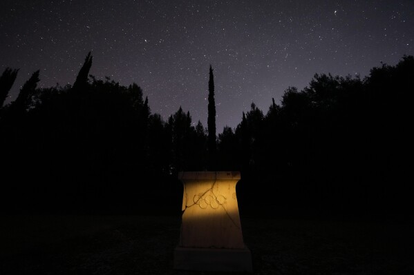 A marble altar with the Olympic rings stands under the night sky at the monument where is placed the heart of French Baron Pierre de Coubertin, in ancient Olympia, on Monday April 8, 2024. Born in 1863, Coubertin was the second president of the IOC — after Greece's Demetrios Vikelas — serving from 1896-1927. His tenure included the games held in Paris in 1900 and 1924. (AP Photo/Petros Giannakouris)