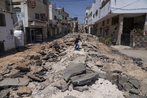 Two Palestinian school boys cross a street damaged during the July Israeli army operation in the West Bank refugee camp of Jenin, Thursday, Aug. 3, 2023. Two months after being cut from the United Nations' main food assistance program, families in the West Bank and Gaza Strip are surviving on one meal a day. The World Food Program suspended all food aid to 60% of its beneficiaries in Gaza and the West Bank in June, marking the largest-ever cut to its funding in the region. (AP Photo/Nasser Nasser)