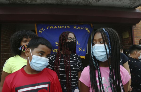 Malik Bey, 11, left, stands with his sisters in front of St. Francis Xavier School in Newark,  on Thursday, Aug. 6, 2020, as parents meet to fight the school's permanent closure. "Give them a shot," said Bey's father, Malik Bey Sr. "My son has been coming here since kindergarten and he's in sixth grade now. This is what he knows, and the kids are who he knows. Let's leave them together." (AP Photo/Jessie Wardarski)