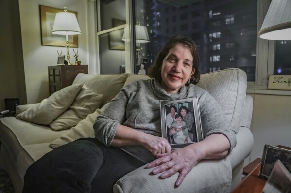 Anne D'Innocenzio shows a portrait of herself, right, with her sister, Donna Burke, left, and mother, Marie D'Innocenzio, as she sits on a sofa from her childhood home, Monday, Feb. 26, 2024, in New York. D'Innocenzio said, "After Mom's passing, my sister and I quickly made a plan to honor her wishes: what to keep, which items to give to relatives and friends, which basic items to donate — and what to just discard." (AP Photo/Bebeto Matthews)