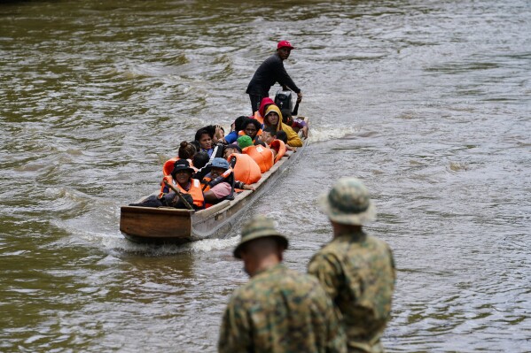 Migrants heading north arrive to Lajas Blancas where a Panamanian border police officer stands on the bank of the Chucunaque River in the Darien province, Panama, Friday, Oct. 6, 2023, after walking across the Darien Gap from Colombia. (AP Photo/Arnulfo Franco)