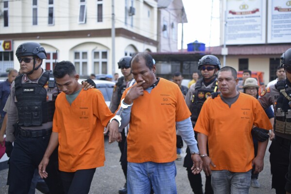Police officers escort suspected human traffickers who were arrested, at the local police headquarters, in Lhokseumawe, Aceh province, Indonesia, Friday, Dec. 8, 2023. Police said they arrested three Aceh residents for human trafficking on Friday. They are suspected of helping 30 Rohingya refugees leave their camp in the city of Lhokseumawe. The suspects were given 1.8 million rupiah ($115) to smuggle the refugees from the camp to the city of Medan in North Sumatra province, said Henki Ismanto, the Lhokseumawe police chief.(AP Photo/Rahmat Mirza)