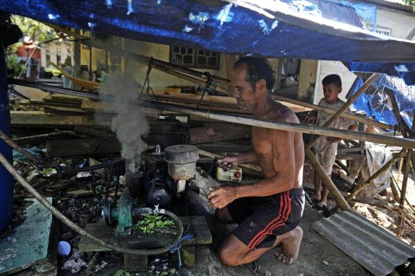 Jembong, a boat maker, powers up the diesel generator he uses for work on Karampuang Island, in West Sulawesi, Indonesia, Thursday, Dec. 22, 2022. For the energy-intensive power tools he uses to handcraft boats from his home, he needs diesel. (AP Photo/Dita Alangkara)
