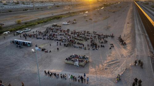 As the sun sets, migrants wait outside a gate in the border fence to enter into El Paso, Texas, to be processed by the Border Patrol, Thursday, May 11, 2023. Migrants rushed across the Mexico border, racing to enter the U.S. before pandemic-related asylum restrictions are lifted in a shift that threatens to put a historic strain on the nation's beleaguered immigration system. (AP Photo/Andres Leighton)