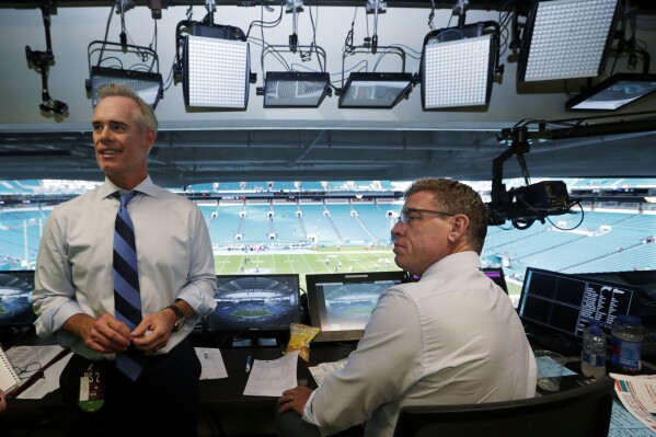 FILE - Fox Sports play-by-play announcer Joe Buck, left, and analyst Troy Aikman work in the broadcast booth before a preseason NFL football game between the Miami Dolphins and Jacksonville Jaguars in Miami Gardens, Fla., Aug. 22, 2019. In their 22nd season together, they have become the NFL's longest-tenured broadcast team. The first 20 years were at Fox before they moved to ESPN's 鈥淢onday Night Football鈥� last year. (AP Photo/Lynne Sladky, File)