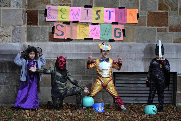 Trick-or-treaters poses in front of sign supporting the Lewiston community, Tuesday, Oct. 31, 2023, at Bates College in Lewiston, Maine, in the wake of last week's mass shootings,. The college hosted a campus-wide Halloween route for youngsters on a candy collecting mission. (AP Photo/Robert F. Bukaty)
