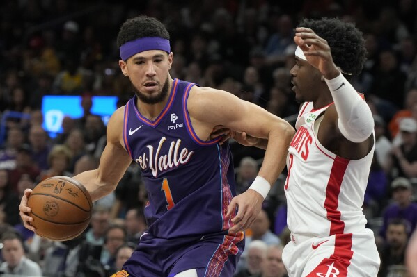 Phoenix Suns guard Devin Booker (1) drives against Houston Rockets guard Aaron Holiday, right, during the first half of an NBA basketball game, Thursday, Feb. 29, 2024, in Phoenix. (AP Photo/Rick Scuteri)