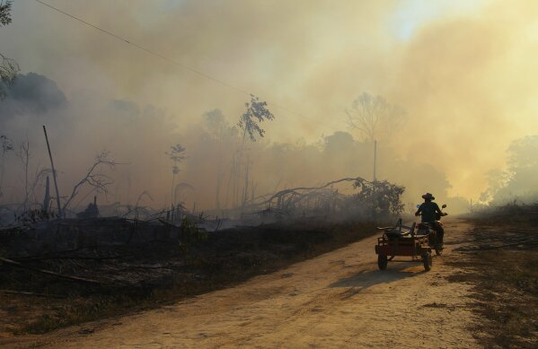 A man rides a motorbike pulling a cart along a paved dirt road in an area scorched by fires near Labrea, Amazonas state, Brazil, Friday, Aug. 7, 2020. According to the National Institute for Space Research, fires in the Brazilian Amazon increased 28% in July from a year ago. Environmentalists have expressed concern at the rise because August traditionally marks the beginning of the fire season in the region. (AP Photo/Edmar Barros)