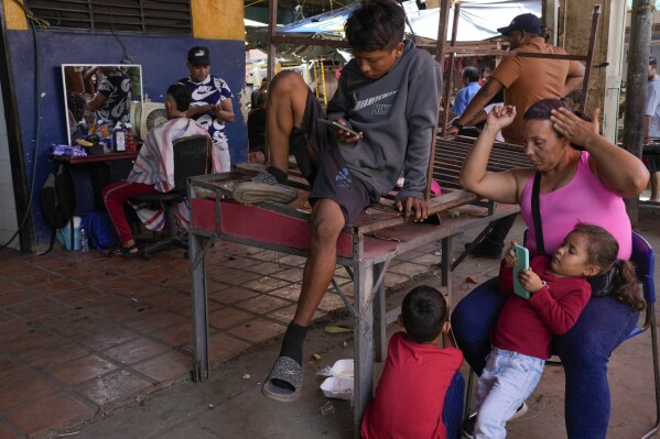 Carla Machado, right, waits with her children for her husband who cuts hair at a flea market in Maracaibo, Venezuela, Monday, July 22, 2024. The country's presidential election is set for July 28. (ĢӰԺ Photo/Matias Delacroix)