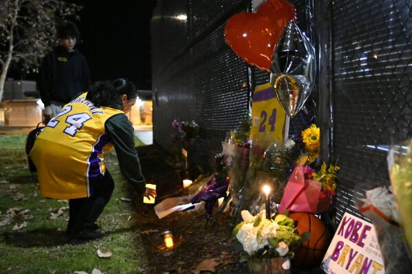 Christina Espinoza places a candle inside a small memorial made in remembrance of former basketball player Kobe Bryant in Calabasas, Calif., Sunday, Jan. 26, 2020, following reports of his death in a helicopter crash in southern California. (AP Photo/Kelvin Kuo)