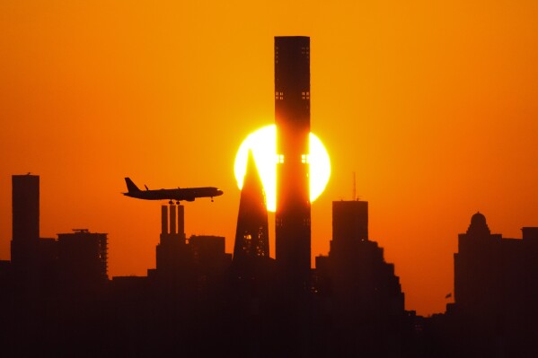 File - The sun sets behind the Manhattan skyline as plane approaches LaGuardia Airport on Sept. 6, 2023, in New York. Holiday travel is kicking off on highways, trains, and airports this week. (AP Photo/Frank Franklin II, File)
