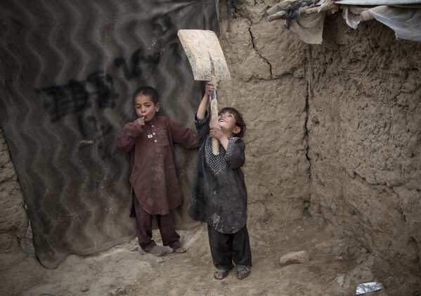 FILE - A young Afghan girl plays with a broken shovel outside her makeshift house at a refugee camp in Kabul, Afghanistan, May 10, 2013. (AP Photo/Anja Niedringhaus, File)