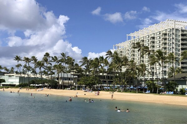 People are seen on the beach and in the water in front of the Kahala Hotel & Resort in Honolulu, Sunday, Nov. 15, 2020. Some locals in the tourism-dependent state have mixed feelings about the return of visitors during the pandemic after enjoying Hawaii beaches with dramatically fewer tourists since March. (AP Photo/Jennifer Sinco Kelleher)