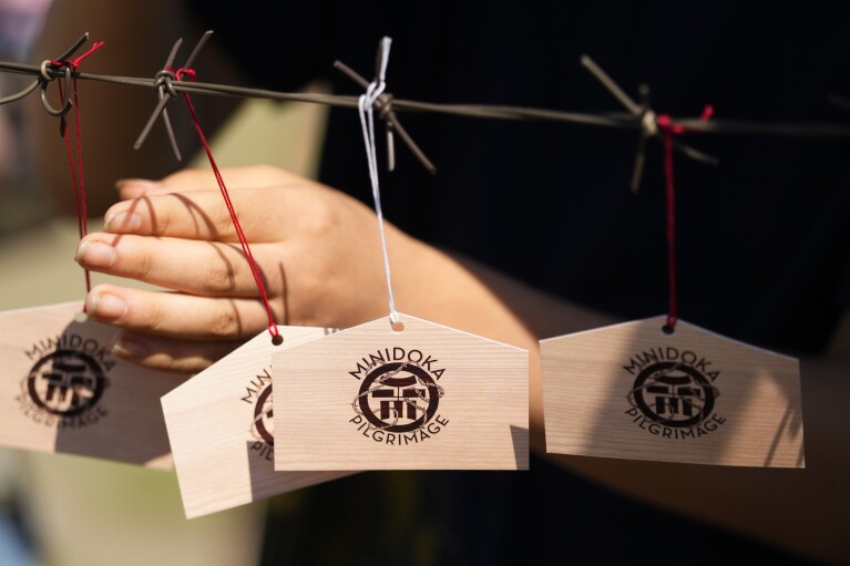 An attendee attaches an "ema," a plaque used to write prayers or wishes in Shinto shrines or Buddhist temples, to a symbolic barbed wire display during a pilgrimage closing ceremony at Minidoka National Historic Site, Sunday, July 9, 2023, in Jerome, Idaho. (AP Photo/Lindsey Wasson)