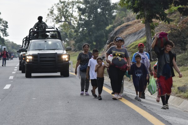 A convoy of National Guard soldiers passes migrants walking north on the side of the highway in Villa Comaltitlan, in the southern Mexican state of Chiapas, Wednesday, Dec. 27, 2023. (AP Photo/Edgar H. Clemente)