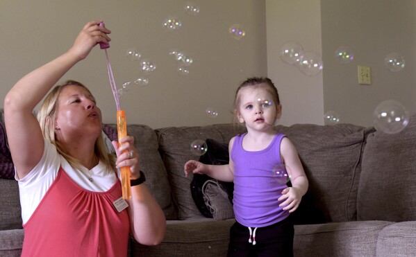 Early Intervention speech pathologist Megan Sanders blows bubbles for 2-year-old Aria Faulkner, while working with her at parents Lindsey and Kendrick Faulkner's home in Peoria, Ill., Aug. 15, 2023. (AP Photo/Ron Johnson)