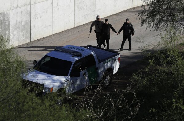 FILE - In this Nov. 16, 2016, file photo, a U.S. Customs and Border Patrol agent walks with suspected immigrants caught entering the country illegally along the Rio Grande in Hidalgo, Texas. The Trump administration has quietly shut down the nation's asylum system for the first time in decades amid coronavirus concerns, largely because holding people in custody is considered too dangerous. (AP Photo/Eric Gay, File)