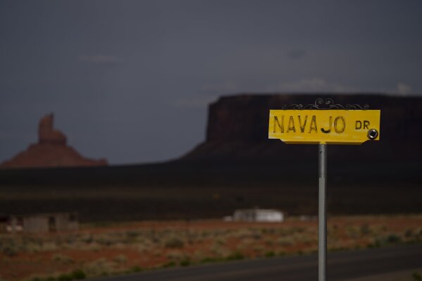 A sign for Navajo Drive is seen against a cloud-darkened Sentinel Mesa in Oljato-Monument Valley, Utah on the Navajo Reservation on April 30, 2020. The reservation has some of the highest rates of coronavirus in the country. If Navajos are susceptible to the virus' spread in part because they are so closely knit, that's also how many believe they will beat it. (AP Photo/Carolyn Kaster)