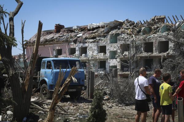Local residents stand next to damaged residential building in the town of Serhiivka, located about 50 kilometers (31 miles) southwest of Odesa, Ukraine, Friday, July 1, 2022. Russian missile attacks on residential areas in a coastal town near the Ukrainian port city of Odesa early Friday killed at least 19 people, authorities reported, a day after Russian forces withdrew from a strategic Black Sea island. (AP Photo/Nina Lyashonok)