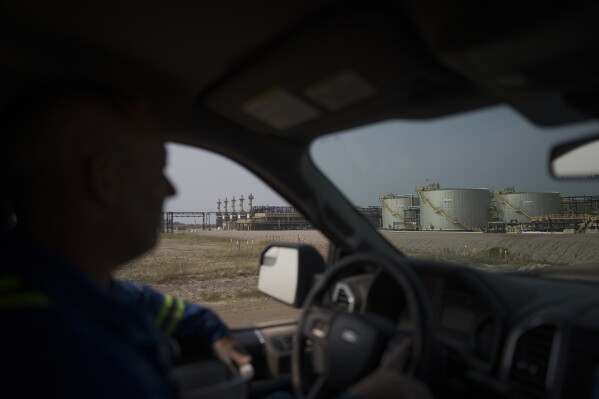 A worker drives by crude oil tanks at Cenovus' Sunrise oil facility northeast of Fort McMurray on Thursday, Aug. 31, 2023. Wildfires are bringing fresh scrutiny to Canada's fossil fuel dominance, its environmentally friendly image and the viability of becoming carbon neutral by 2050. (AP Photo/Victor R. Caivano)
