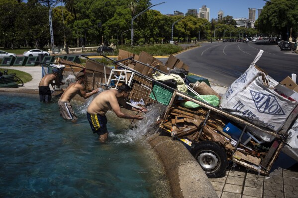 "Cartoneros" soak their cardboard waste with water before taking it to be weighed at a recycling center, while cooling off in a fountain in Buenos Aires, Argentina, Monday, Dec. 11, 2023. South America's second largest economy is suffering 143% annual inflation and four in 10 Argentines are impoverished. (AP Photo/Rodrigo Abd)