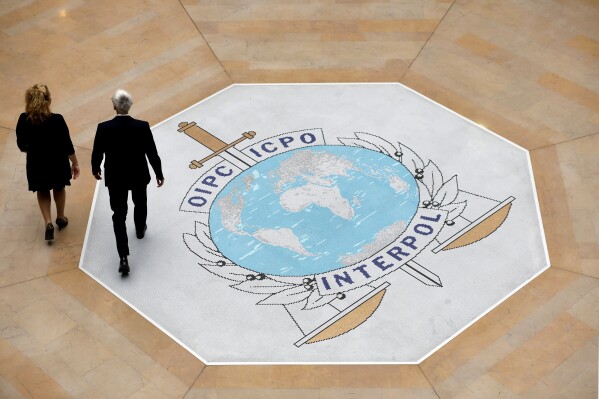 FILE - People walk on the Interpol logo at the international police agency headquarters in Lyon, central France, Thursday Nov. 8, 2018. Interpol said Tuesday, June 4, 2024, it has carried out an anti-corruption operation in the eastern European country of Moldova targeting attempts to sabotage its Red Notice system. The international policing agency, headquartered in Lyon, France, issued a communique stating the move followed the detection of a “small number” of attempts to “block and delete” Red Notices, a critical tool that flags fugitives to law enforcement worldwide. (AP Photo/Laurent Cipriani, File)
