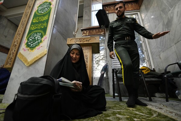 A woman fills out her ballot as a policeman walks past during the parliamentary and Assembly of Experts elections at a polling station in Tehran, Iran, Friday, March 1, 2024. Iran held the country's first election since the mass 2022 protests over mandatory hijab laws after the death in police custody of Mahsa Amini, with questions looming over just how many people will turn out at the polls. (AP Photo/Vahid Salemi)