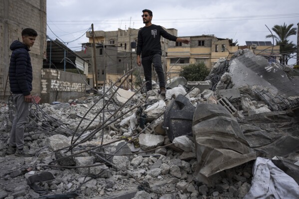 Ibrahim Hassouna, center, the sole survivor of his family, stands amid the rubble of his bombed home in Rafah, southern Gaza Strip, Tuesday, February 13, 2024. On Monday, February 12, Hassouna lost eight members of his family, including three children and says the house was bombed. During an Israeli operation to rescue hostages held in a building in another part of the city.  (AP Photo/Fathima Shabir)