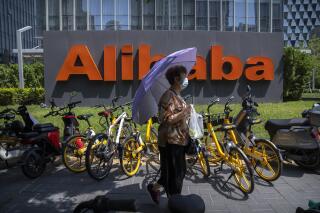A woman holds an umbrella as she walks past the offices of Chinese e-commerce firm Alibaba in Beijing on Aug. 10, 2021. China is tightening control over data gathered by companies about the public under a law approved Friday, Aug. 20, 2021 by its ceremonial legislature, expanding the ruling Communist Party's crackdown on internet industries. The data protection law follows anti-monopoly and other enforcement actions against companies including e-commerce giant Alibaba and games and social media operator Tencent that caused their share prices to plunge. (AP Photo/Mark Schiefelbein)