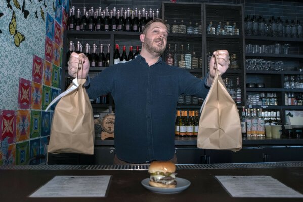 Josh Phillips, the co-owner of Espita, a stylish Mexican restaurant, displays a Ghostburger at his restaurant in downtown Washington, Monday, Feb. 15, 2021. Phillips opened a delivery-only brand called Ghostburger in August to keep Espita’s kitchen running through the winter. He chose burgers because he wanted to reach new customers at a lower price point than Espita. It’s been so successful that Phillips is now scouting for locations for standalone Ghostburger restaurants. (AP Photo/Jose Luis Magana)