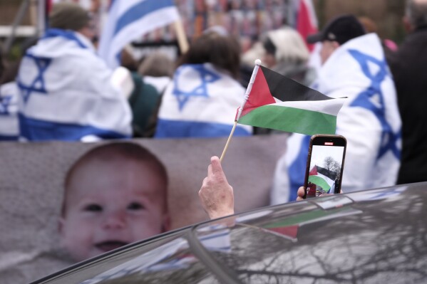 A person waves a palestinian flag while passing a pro-israel protest outside the International Court of Justice in The Hague, Netherlands, Friday, Jan. 12, 2024. The United Nations' top court opened hearings Thursday into South Africa's allegation that Israel's war with Hamas amounts to genocide against Palestinians, a claim that Israel strongly denies. (AP Photo/Patrick Post)