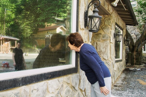 Novelist Rose Senehi peeks into the window of a flood-damaged shop on Main Street in Chimney Rock Village, N.C., on Tuesday, May 13, 2025. (AP Photo/Allen G. Breed)