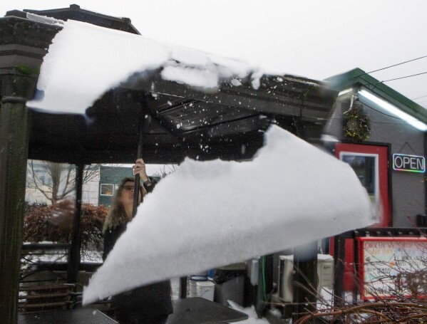Kacey Miller of Quick Fix Coffee Company in Eugene, Ore., knocks snow and ice from the roof of their outdoor seating area along Willamette Street on Wednesday, Jan. 17, 2024. (Chris Pietsch/The Register-Guard via AP)