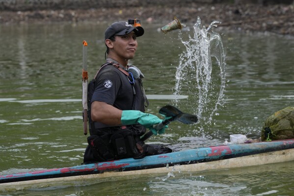 Environmental activist Giri Marhara picks up trash while paddling a kayak at Setu Gede lake in Bogor, West Java, Indonesia, Tuesday, Oct. 10, 2023. Young people like Marhara have been at the forefront of environmental and climate change movements in recent years: initiatives like school strikes for climate action, protests at United Nations climate talks and around the world, and local clean ups have often been youth-led. (AP Photo/Achmad Ibrahim)