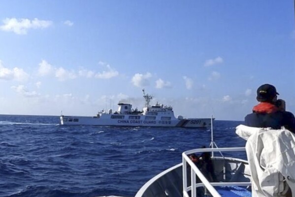 In this photo provided by the Philippine Coast Guard, a Chinese coast guard ship, top, tries to block a Philippine government vessel at the disputed South China Sea on Thursday March 21, 2024. Chinese coast guard ships, backed by a military helicopter, tried to dangerously block but failed to stop two Philippine government vessels carrying scientists from reaching two barren sandbars called Sandy Cay in the disputed South China Sea, Philippine officials said Friday. (Philippine Coast Guard via AP)